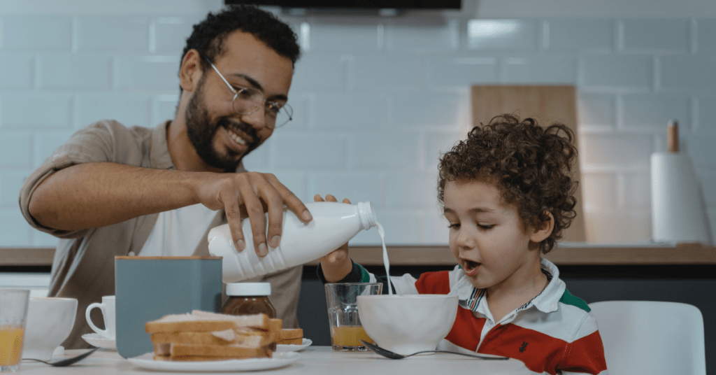 dad present with child at breakfast, pouring his milk 