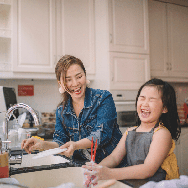 girl washing dishes with mother