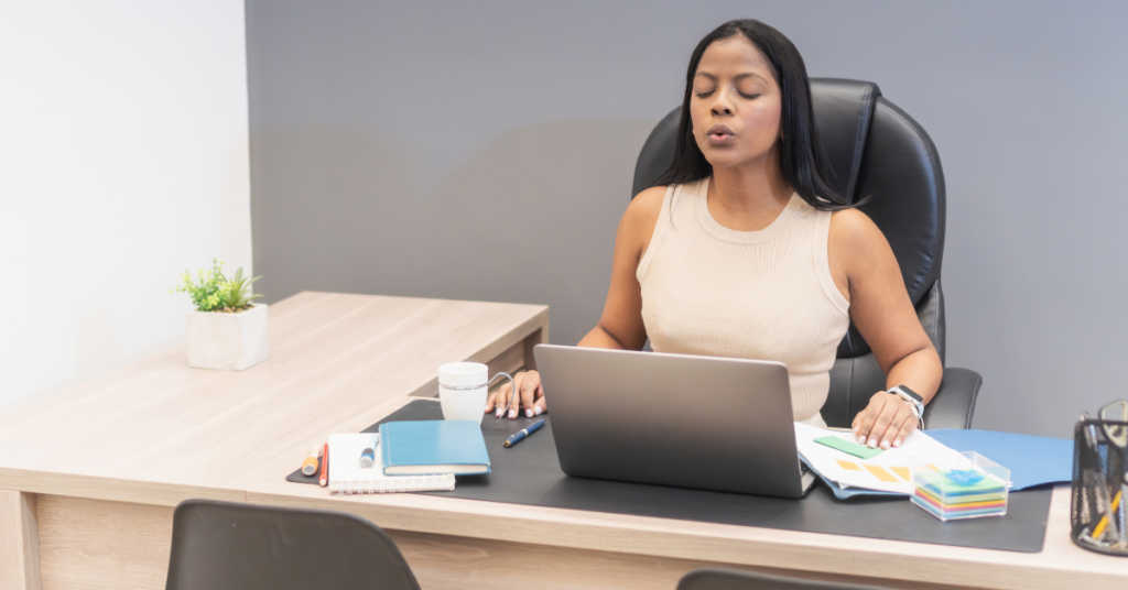 A teacher inspiring love in the classroom as she sits at her desk and takes a deep calming breath in order to stay regulated, modeling how to calm down for her students